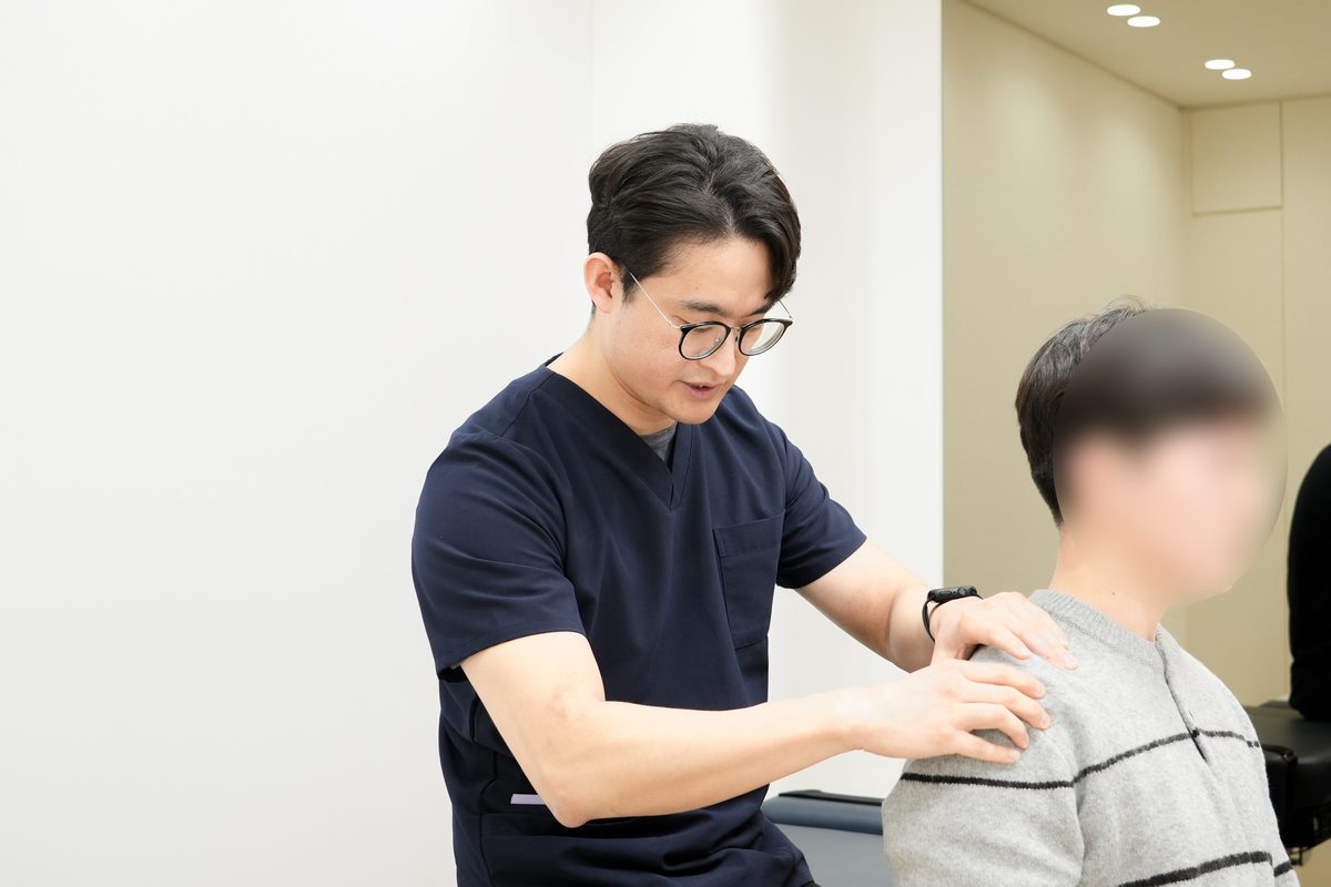 앉은 자세의 환자 어깨에 양손을 대고 좌우 어깨 높이와 견갑 주변 긴장을 촉진하는 오종석 대표원장 - 마포당한의원 추나 진찰