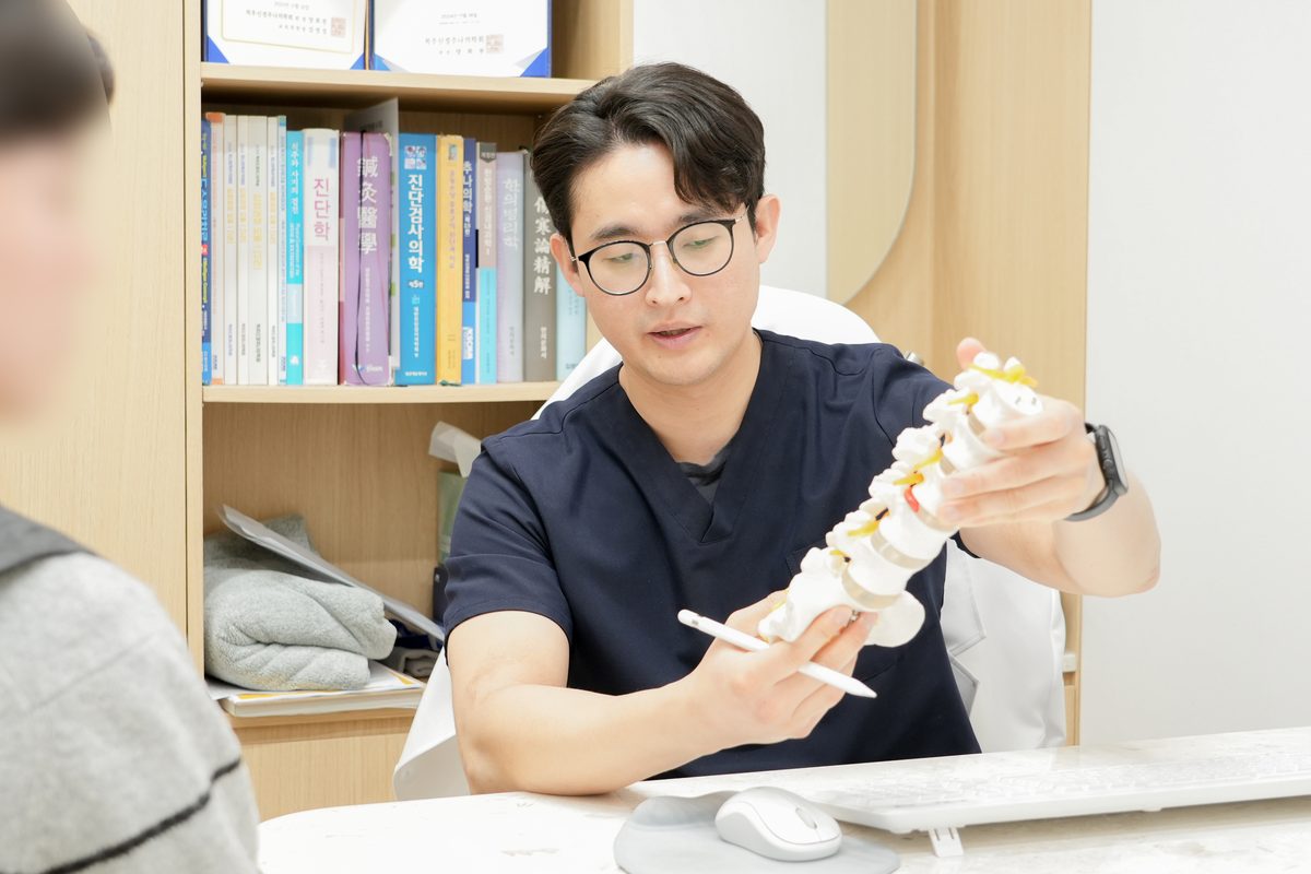 오종석 대표원장이 요추 모형으로 추간판과 후관절 구조를 짚으며 추나치료 방향을 설명하는 장면 - 마포당한의원