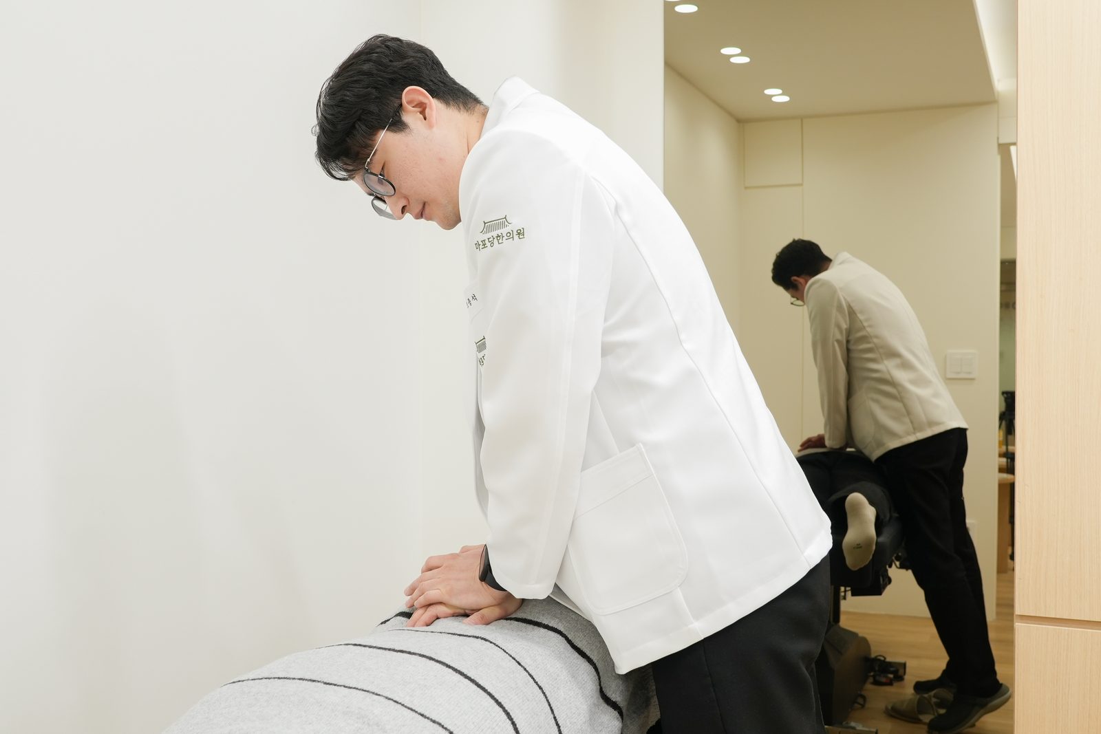 흰 가운을 입은 한의사가 엎드린 환자의 허리 마디에 손을 대고 추나치료를 하는 장면 - 마포당한의원 마포 한의원 추나