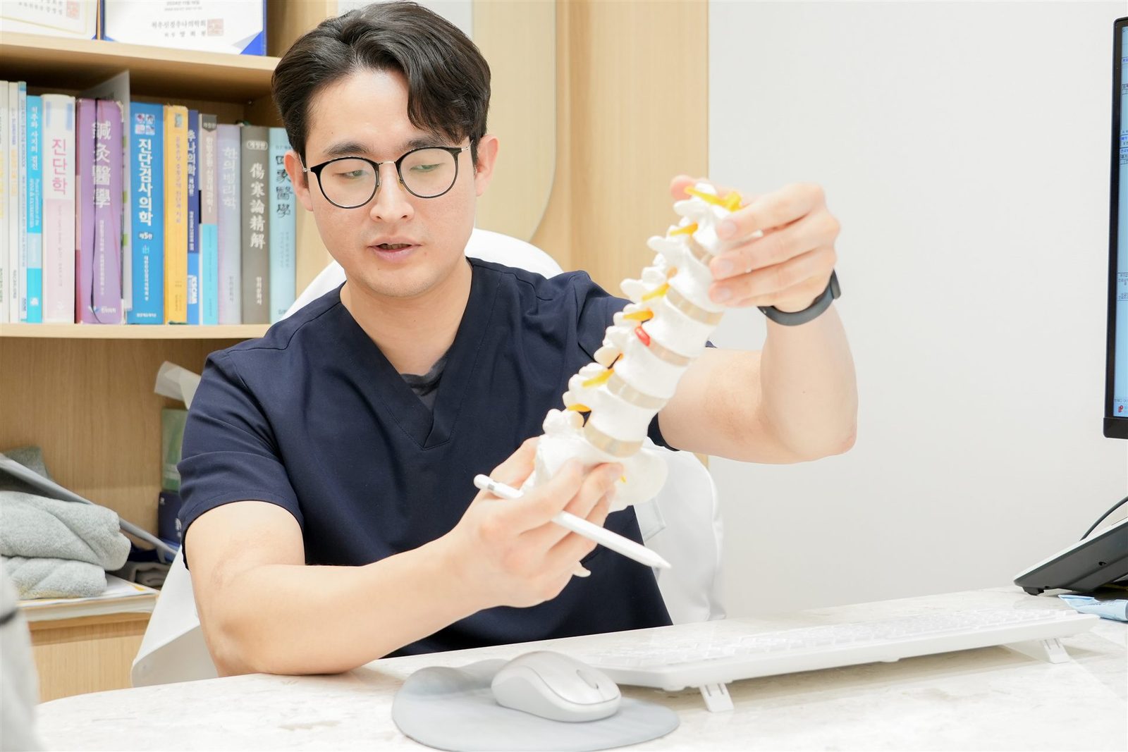 한의사가 요추 모형을 들고 환자에게 척추 상태와 추나치료 시점을 설명하는 상담 장면 - 마포당한의원 추나 클리닉