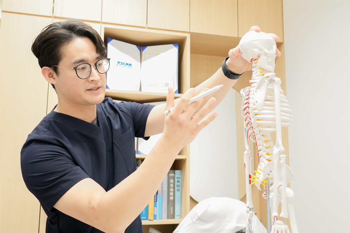 한의사가 척추 골격 모형으로 요추 신경 압박을 설명하는 모습 - 마포당한의원 다리 저림·당김